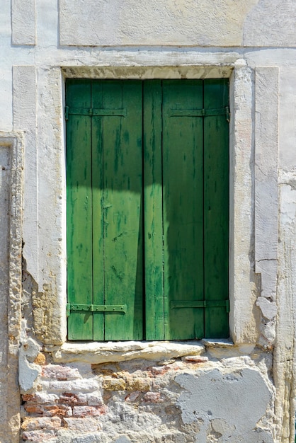 Grünes Fenster auf rissiger Betonwand mit Blick auf rote Backsteine