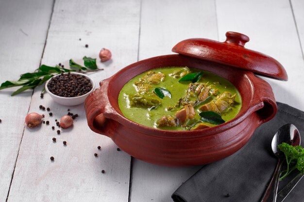 Grünes Hühnchen-Curry mit rohen Zutaten, das in einem Tongeschirr angerichtet wird