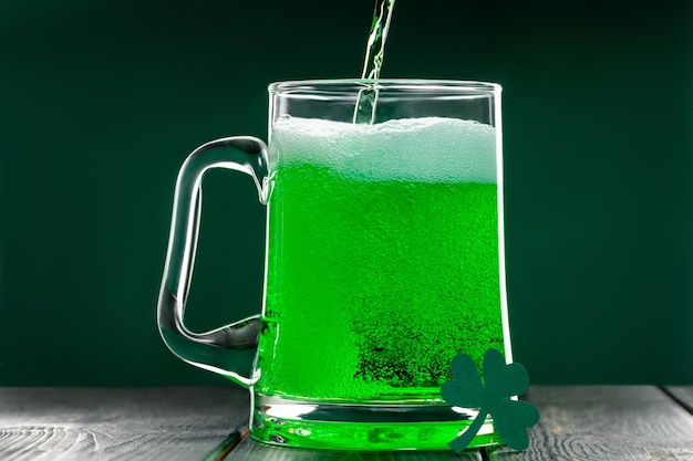 Grünes irisches Bier wird in einen Becher auf dunklem Hintergrund gegossen, um den St. Patrick's Day zu feiern