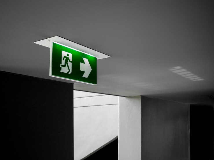Foto grünes notausgangsschild, das von der decke hängt, die am dunklen korridor nahe der feuerleiter-tür im gebäude leuchtet