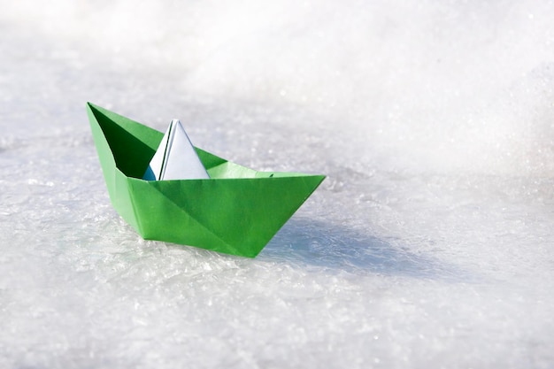 Grünes Papierboot auf Schnee