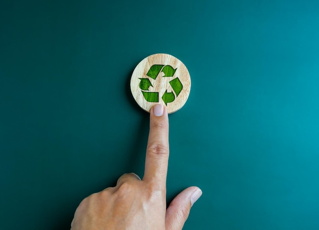 Grünes Recycling-Symbol auf rundem Holzblock, das von Hand auf blauem Hintergrund zeigt Ökologische Nachhaltigkeitskooperation Reduzierung der Wiederverwendung und Recyclingkonzepte Kampagne für grünes Recycling