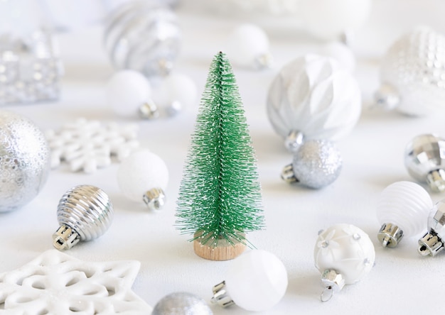 Grünes Spielzeug Weihnachtsbaum mit weißen und silbernen Weihnachtsschmuck Nahaufnahme auf weißem Tisch. Monochrome Winterkomposition