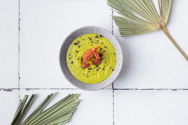 Grünes Suppenpüree mit gegrilltem Speck auf Fliesenhintergrund-Palmenblättern hochwertiges Foto