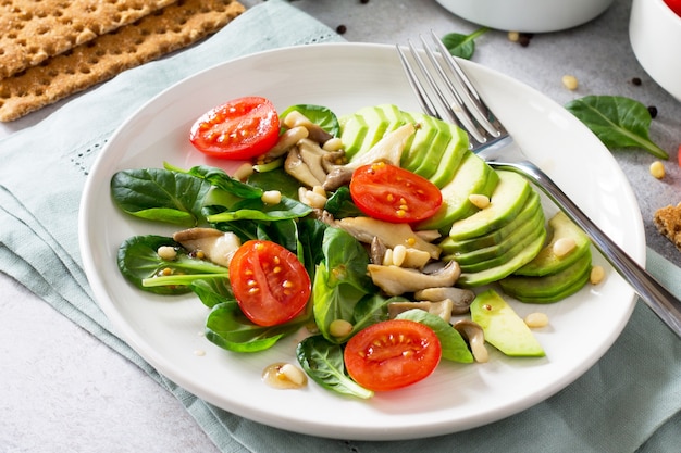 Grünes vegetarisches Frühstück in einer Schüssel mit Avocadopilzen, Kirschtomaten, Pinienkernen, Spinat und Dressing mit Vinaigrettesauce Diätkonzept von vegetarischem Essen