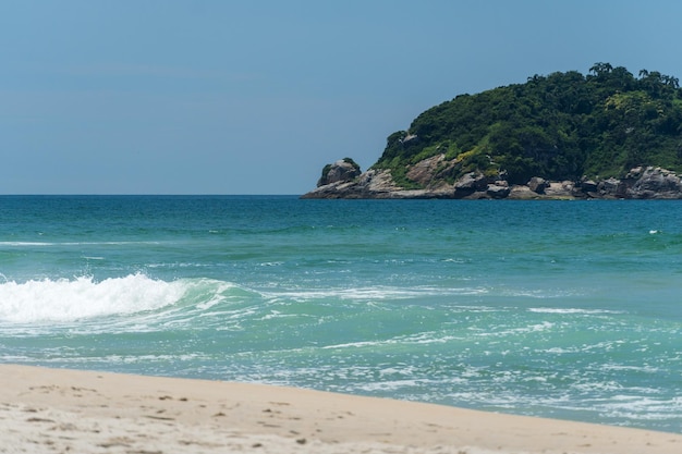 Grumari-Strand in der Nähe von Barra da Tijuca in Rio de Janeiro, Brasilien. Sonniger Tag mit blauem Himmel, klarem Wasser und kleinen Wellen. Hügel und Natur rundherum.