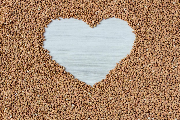 Grumos de trigo sarraceno em uma tigela em forma de coração sobre fundo branco de madeira