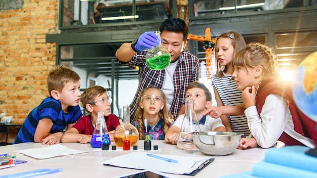 Grundschüler achten sorgfältig auf ihren Lehrer, der interessante chemische Experimente mit farbigen Flüssigkeiten in Glasflocken zeigt.