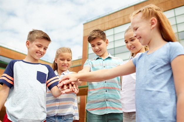 grundschulbildung, freundschaft, kindheit und menschenkonzept - gruppe glücklicher grundschüler mit den händen an der spitze im freien