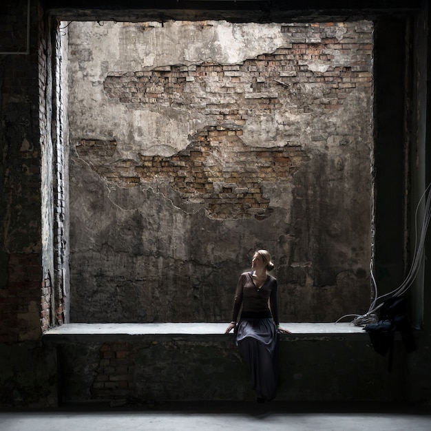 Foto grungy vista de mujer solitaria sentada en la ventana grande en el antiguo edificio abandonado