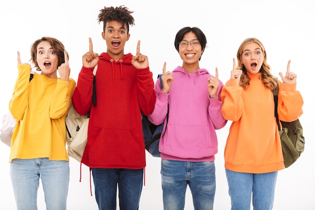 Foto grupo de adolescentes alegres aislados, llevando mochilas, apuntando hacia arriba