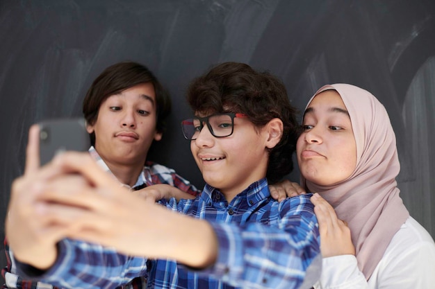 grupo de adolescentes árabes tomando una foto selfie en un teléfono inteligente con pizarra negra en el fondo