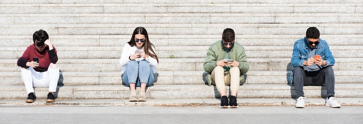 Grupo de adolescentes concentrados en teléfonos y manteniendo distancia