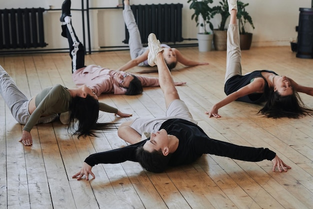 Grupo de adolescentes contemporáneos en ropa deportiva elegante haciendo ejercicio en el suelo