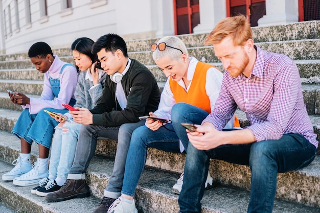 Grupo de adolescentes navegando con los teléfonos inteligentes sentados juntos al aire libre