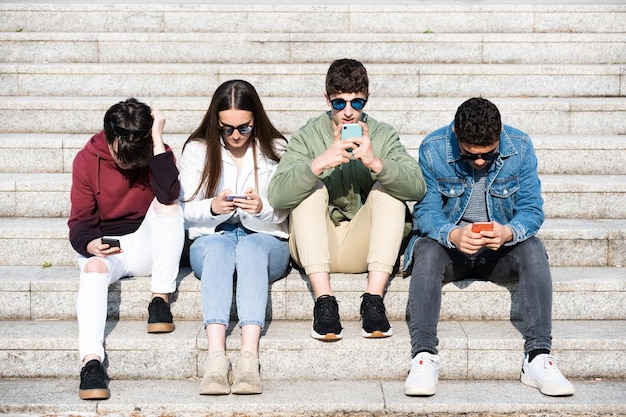 Grupo de adolescentes sentados en las escaleras y concentrados en los teléfonos