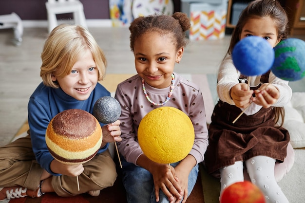 Grupo de adorables niños multiculturales que estudian planetas del sistema solar mientras sostienen sus modelos en