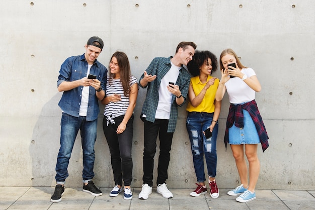 Grupo de adultos jóvenes al aire libre usando teléfonos inteligentes juntos y refrigeración
