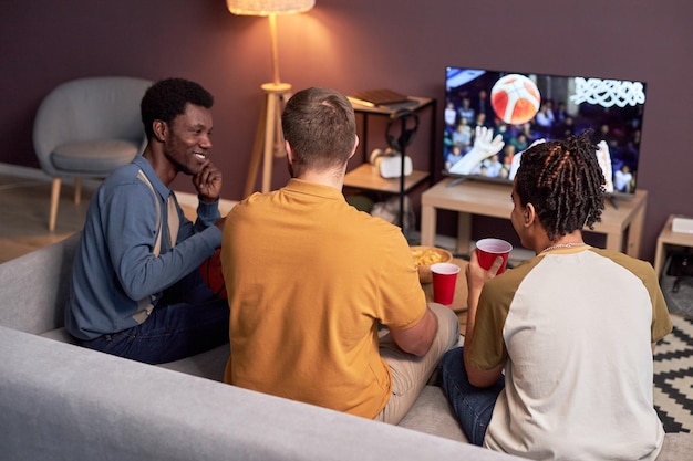 Grupo de aficionados al deporte viendo el partido de baloncesto en casa en la televisión y animando