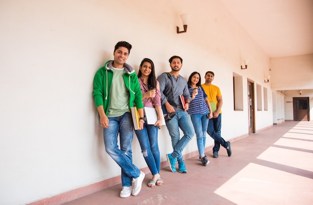 Grupo alegre de jovens indianos asiáticos de estudantes universitários ou amigos rindo juntos enquanto estão sentados, em pé ou caminhando no campus