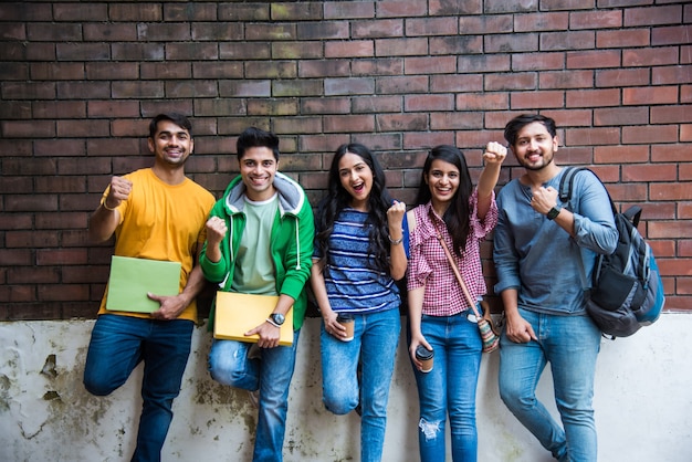 Grupo alegre de jovens indianos asiáticos de estudantes universitários ou amigos rindo juntos enquanto estão sentados, em pé ou caminhando no campus