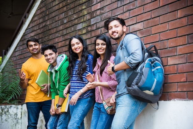 Grupo alegre de jovens indianos asiáticos de estudantes universitários ou amigos rindo juntos enquanto estão sentados, em pé ou caminhando no campus