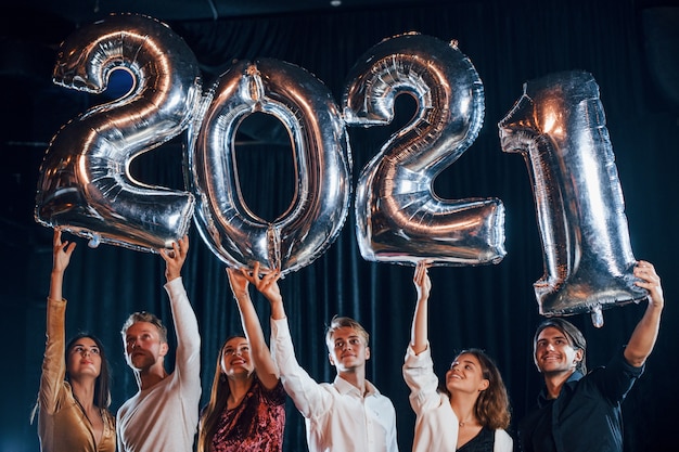 Grupo alegre de pessoas com bebidas e balões nas mãos, comemorando o novo ano de 2021.