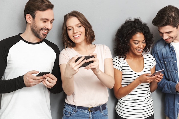 Grupo alegre emocional de amigos usando teléfonos móviles mirando a un lado.