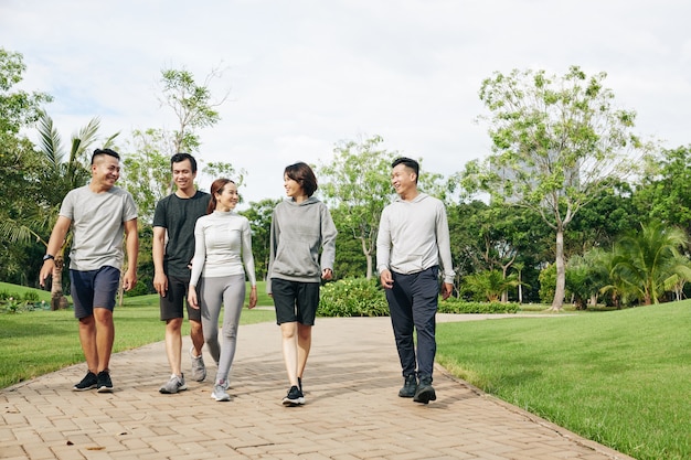 Grupo de alegres hombres y mujeres vietnamitas en forma caminando en el parque y discutiendo el entrenamiento al aire libre que acaban de tener