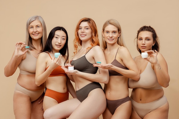Foto grupo de alegres mujeres multirraciales diferentes con lencería sexy sosteniendo frascos de crema
