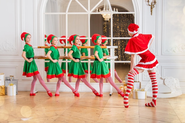 Un grupo de alegres niños felices, niñas, novias, estudiantes de una escuela coreográfica profesional con disfraces de elfos bailan con regalos en el fondo de un árbol de Navidad