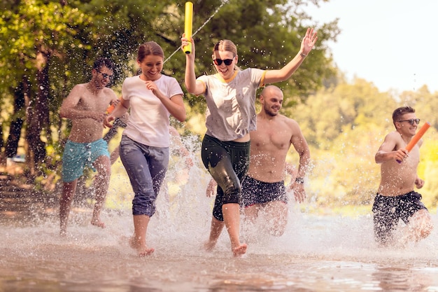 Grupo de alegría de verano de amigos felices divirtiéndose mientras corren y chapotean en el río