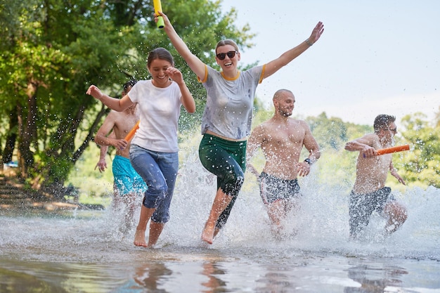 Grupo de alegría de verano de amigos felices divirtiéndose mientras corren y chapotean en el río