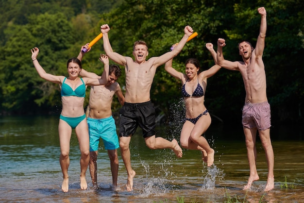 Grupo de alegría de verano de amigos felices divirtiéndose mientras corren y chapotean en el río