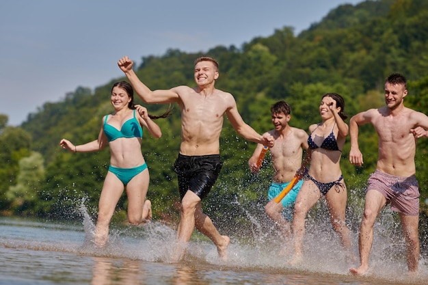 Grupo de alegría de verano de amigos felices divirtiéndose mientras corren y chapotean en el río