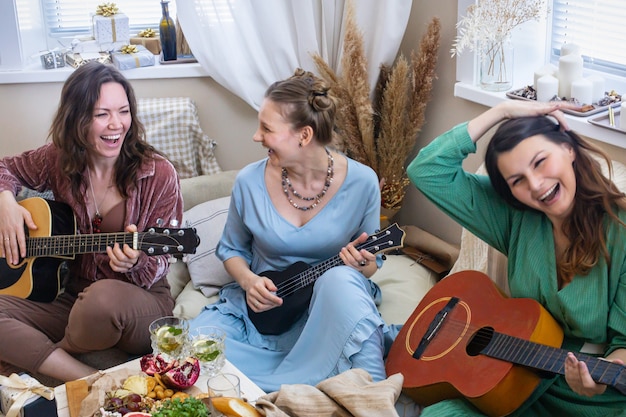 Grupo de amigas tocando la guitarra cantando canciones divirtiéndose en henparty en estilo bohemio hippie