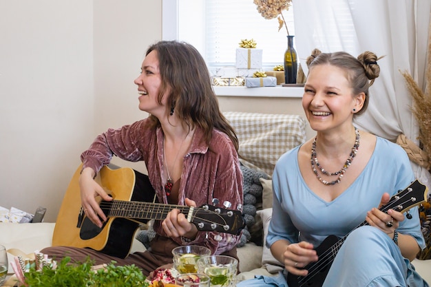 Grupo de amigas tocando la guitarra cantando canciones divirtiéndose en henparty en estilo bohemio hippie