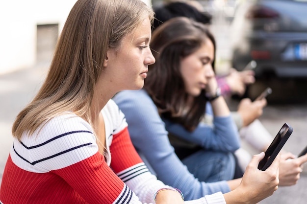 Grupo de amigos aburridos usando un teléfono inteligente sentado en el patio trasero de la universidad Jóvenes adictos al teléfono inteligente Concepto de vida triste de tecnología con estudiantes siempre conectados Filtro de contraste