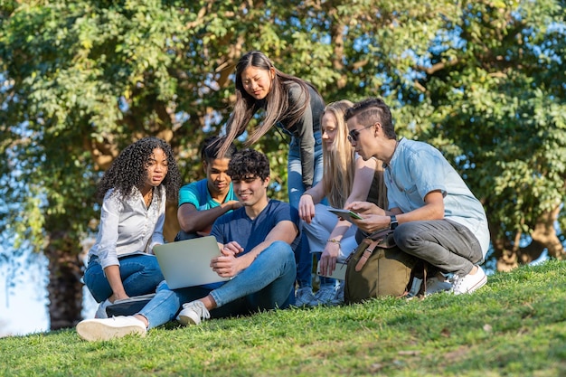 Grupo de amigos adolescentes mirando la computadora portátil en el parque sobre hierba verde Tres niños y tres niñas