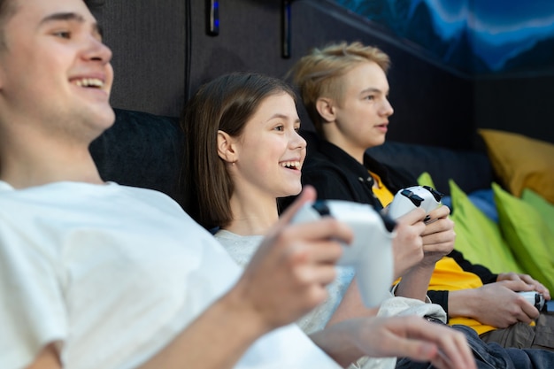 Grupo de amigos de adolescentes, niños y niñas jugando videojuegos en una consola en un club de juegos.