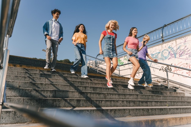 Grupo de amigos adolescentes sonrientes que usan camisetas coloridas hablando comunicación caminando por la calle