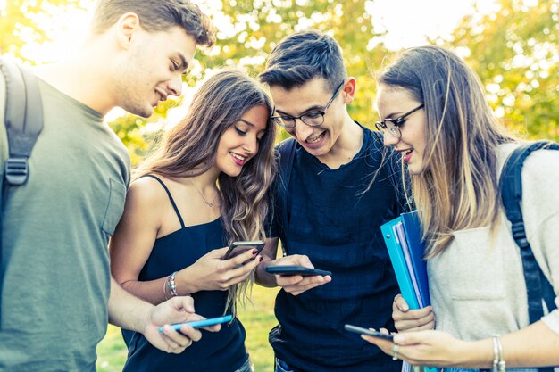 Grupo de amigos adolescentes con teléfonos inteligentes en el parque