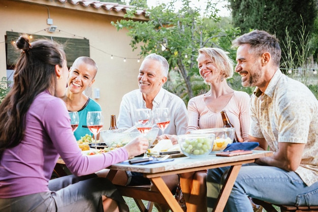 Grupo de amigos adultos maduros brindando por sus copas de vino y cervezas y divirtiéndose en una cena