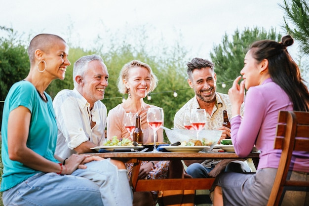 Grupo de amigos adultos o familiares hablando y divirtiéndose sentados a la mesa en una cena en un patio trasero