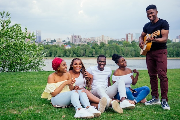 Grupo de amigos afroamericanos felices sonrientes amigos tocando la guitarra al aire libre picnic en la campaña