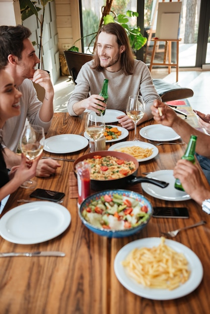 Grupo de amigos alegres comiendo y hablando en la mesa