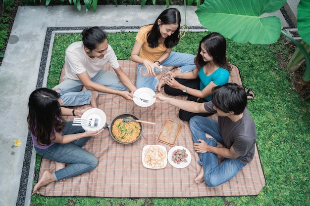 Grupo de amigos asiáticos divirtiéndose mientras come y bebe en el patio trasero