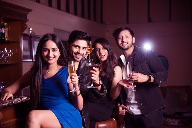 Grupo de amigos asiáticos indios sentados en el lounge bar, tomando bebidas o cócteles, celebrando año nuevo, cumpleaños o éxito