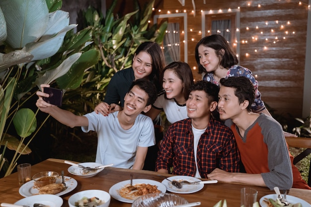 El grupo de amigos asiáticos se toma una selfie con un teléfono inteligente mientras tiene una fiesta en el jardín