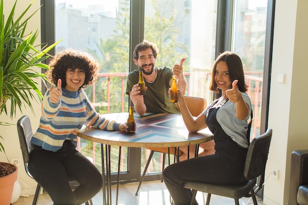 Foto grupo de amigos bebiendo cervezas, relajados y felices en casa nueva